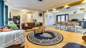 Een ruime woonkamer met een leren bank, een ronde salontafel en een vloerkleed met een patroon. Er is een eethoek met een houten tafel en stoelen.