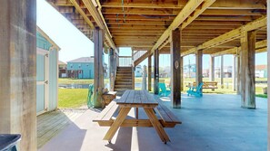 A wooden deck with a picnic table, outdoor seating, and a staircase leading to an upper level. - Blue Seagull: 2 BR, 2 BA House in Crystal Beach, Sleeps 7 (Bolivar Peninsula)