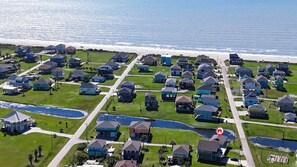 An aerial view of a coastal residential area with houses, a beach, and a waterway. - Blue Seagull: 2 BR, 2 BA House in Crystal Beach, Sleeps 7 (Bolivar Peninsula)