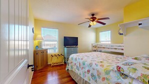 Un dormitorio con una cama individual superior e inferior, ventilador de techo, televisión sobre un mueble y ventana con persianas.