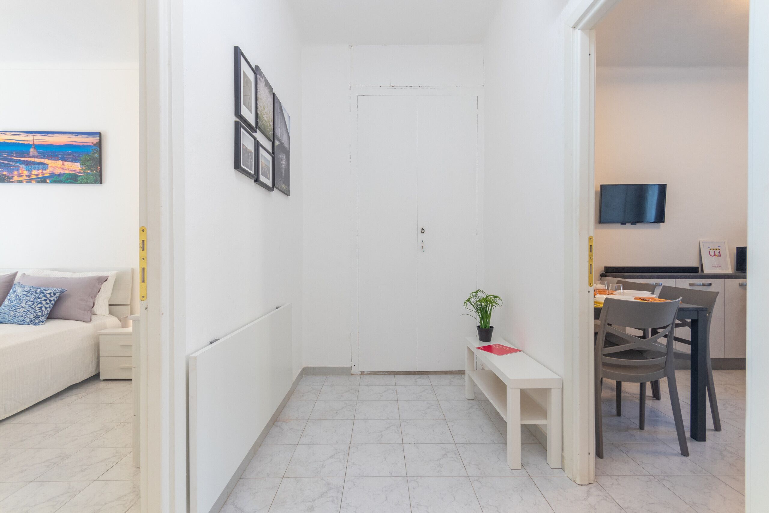 Un appartement moderne et bien éclairé, avec un intérieur blanc, un coin repas comprenant une table et des chaises, un petit banc et un téléviseur fixé au mur.