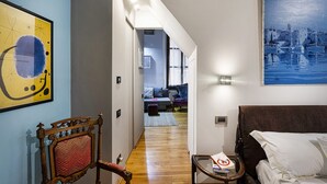A hotel room with a wooden floor, a bed, a chair, a small table, and a painting on the wall. - Alle Mura del Molo Apartment by Wonderful Italy (Genova)