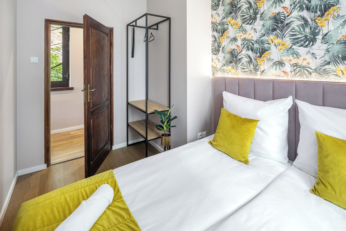 Un dormitorio con una cama, un armario, una planta y un papel tapiz de motivos tropicales.