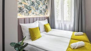 A double bed with white and yellow bedding, a potted plant, and a tropical wallpaper. - Garden House Apartments (Kraków)