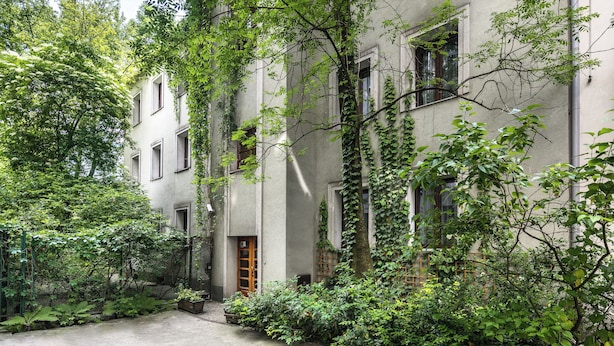 A building with a courtyard surrounded by lush greenery and a wooden door. - Garden House Apartments (Kraków)