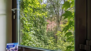 A window with a view of a brick wall and dense foliage. - Garden House Apartments (Kraków)