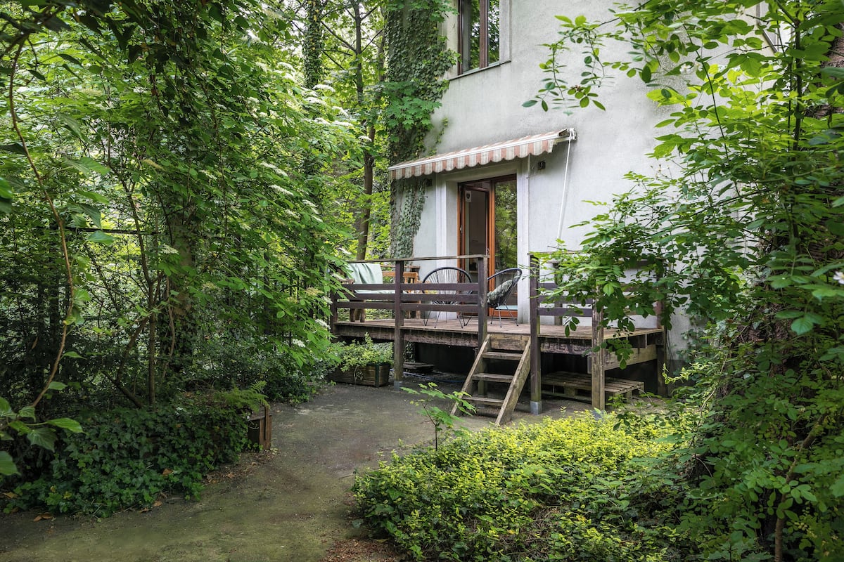 Une terrasse en bois rustique, avec une chaise, une petite table en bois et une échelle menant à un bâtiment doté d’une porte et de fenêtres.
