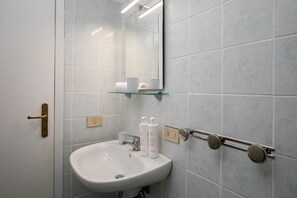 Une salle de bain avec un lavabo blanc, une étagère en verre au-dessus et un miroir.