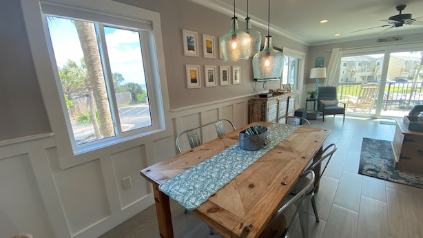 Comedor con mesa de madera, sillas, lámparas colgantes y vistas al exterior a través de amplios ventanales.