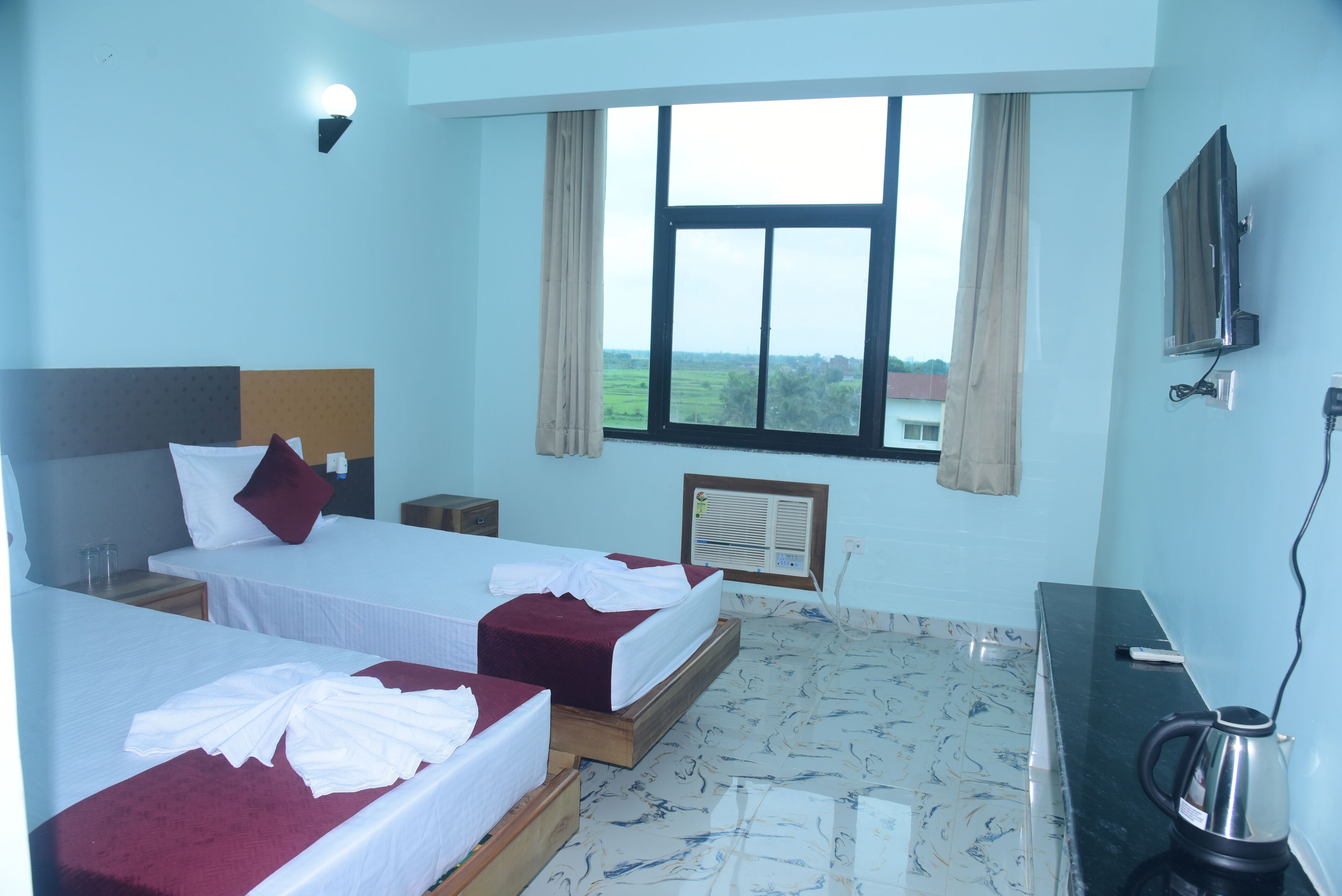 Habitación de hotel con dos camas, televisión, escritorio y ventana con vistas al campo.