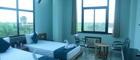 A hotel room with two beds, a small table, chairs, and a desk.