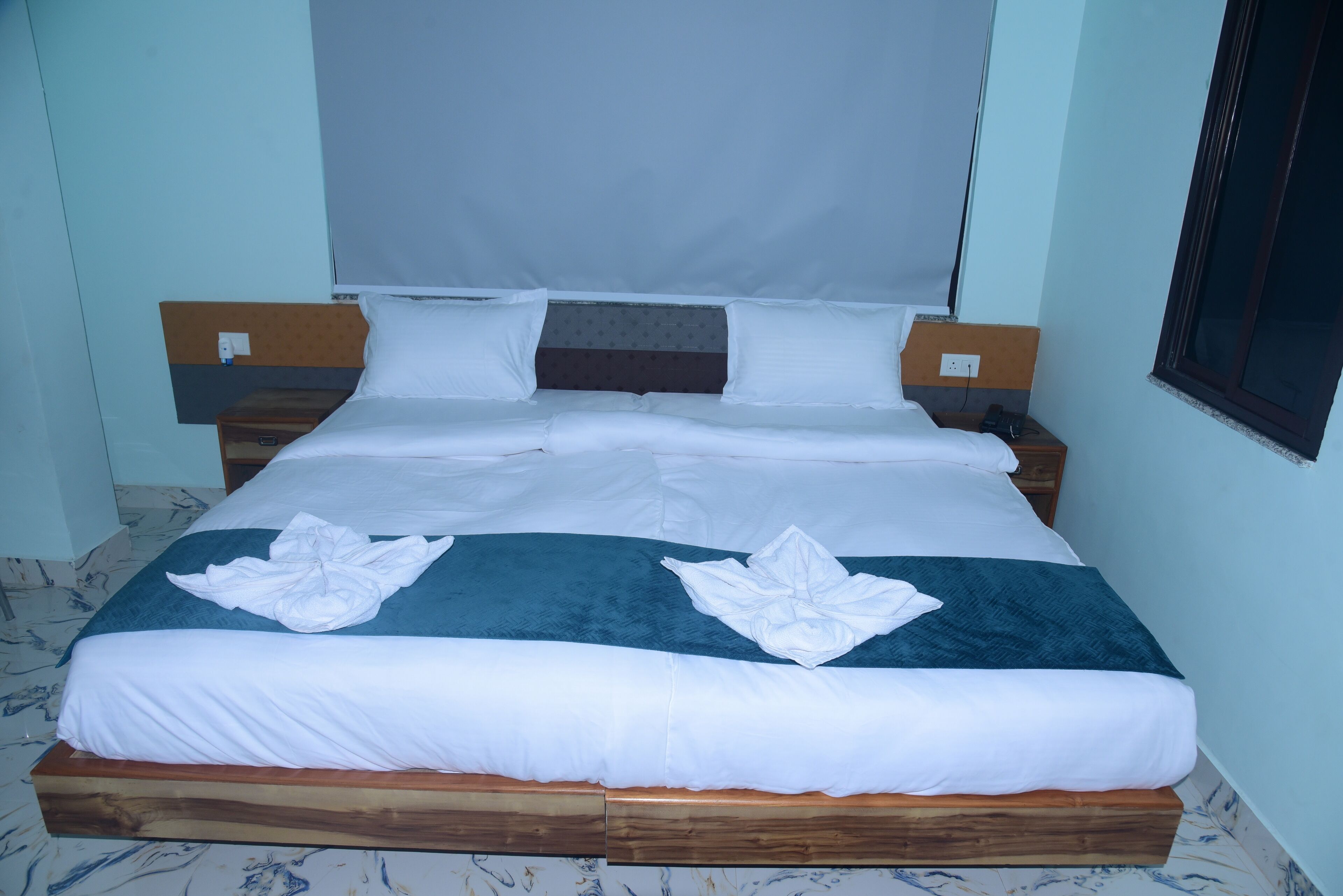 A neatly made bed with white linens and a blue accent, a wooden headboard, and a bedside table with a lamp.
