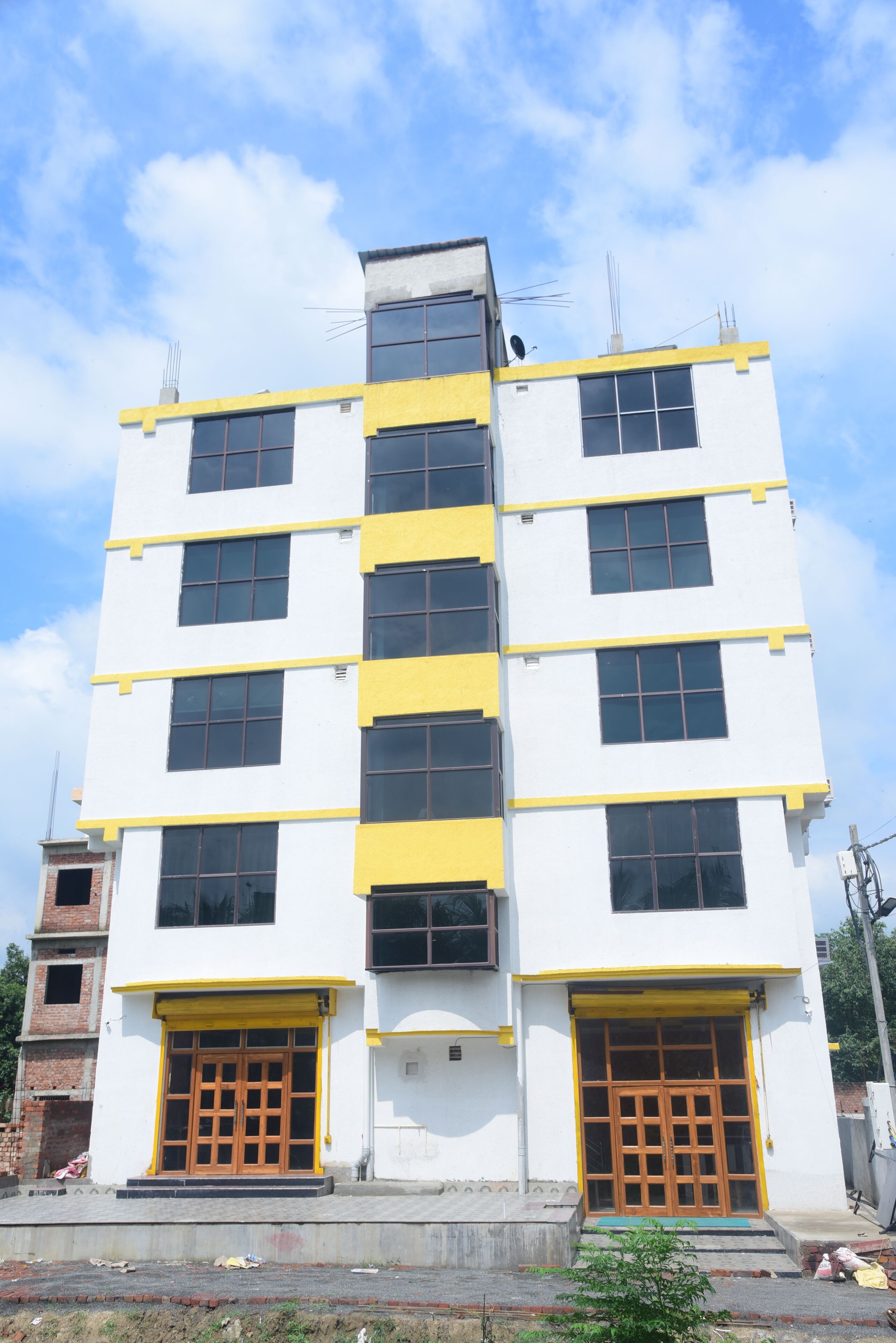 A multi-story building with a white facade and yellow accents, featuring large windows and a central entrance.