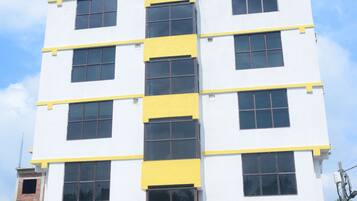 Un edificio de varios pisos con fachada blanca y detalles amarillos, que cuenta con amplios ventanales y una entrada central.