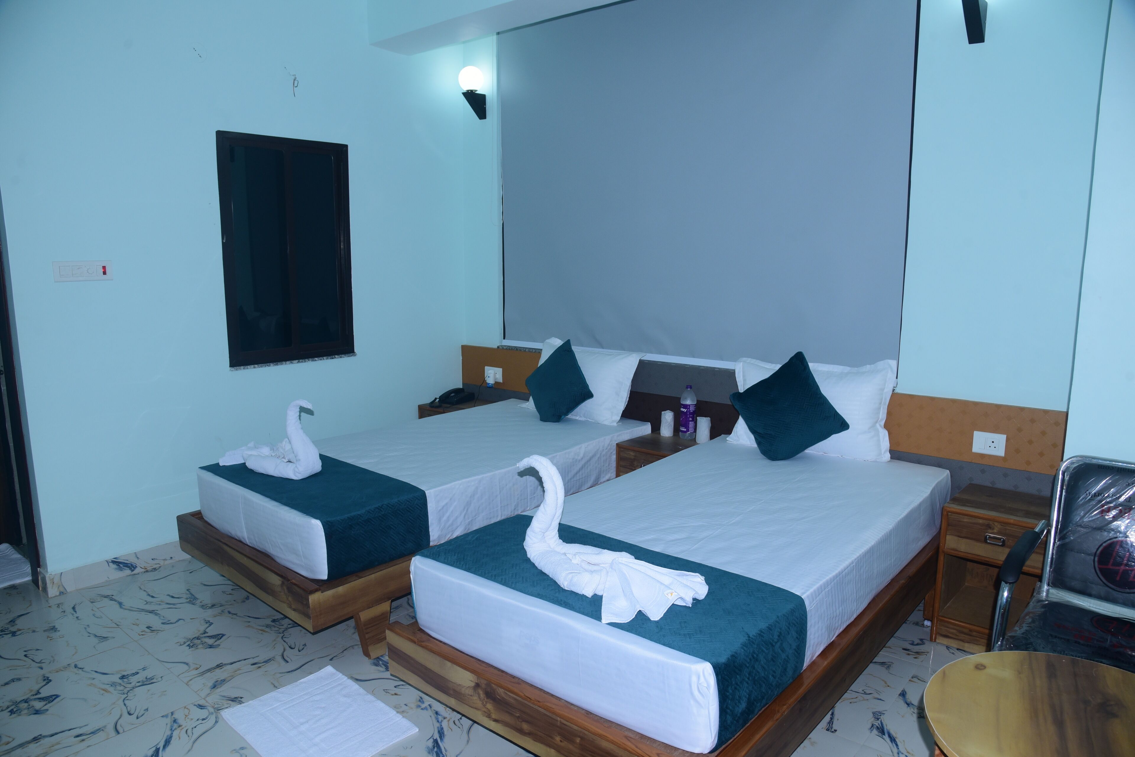 A hotel room with two beds, each with a swan-shaped towel, a bedside table with a lamp, and a chair.
