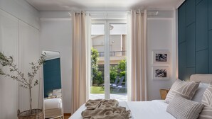 Et soveværelse med en stor seng, udsigt til en balkon, en fletkurv og et spejl.
