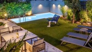 En baghave med swimmingpool, udendørs møbler og en velholdt græsplæne.