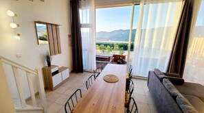 Enjoy meals at the large dining table surrounded by comfortable chairs, with a sofa and additional seating area accessible through the glass door.