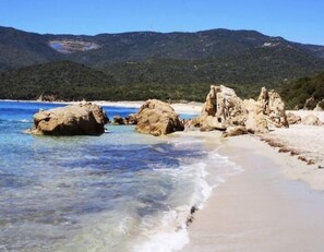 Enjoy the serene coastal landscape with a sandy beach and clear waters, surrounded by rugged rocks and rolling hills.