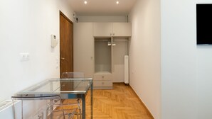 Une pièce moderne et minimaliste, dotée d’une table à manger en verre, d’un plancher en bois, d’une armoire intégrée et d’un téléviseur à écran plat fixé au mur.