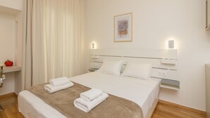 Une chambre d’hôtel avec un lit, du linge de lit blanc, un plaid marron, deux lampes de chevet, une œuvre d’art encadrée au mur et un fruit rouge posé sur une étagère.