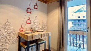 Ein Zimmer mit Holzbalkendecke, einem Tisch mit Glasplatte und Blick auf ein Gebäude durch ein großes Fenster.