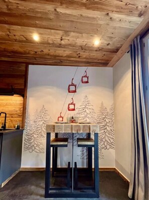 Una stanza accogliente con soffitto in legno, un murale raffigurante una montagna innevata e un tavolo con piano in vetro.