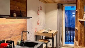 Eine moderne Küche mit Holzbalkendecke, einer integrierten Kochinsel mit Kaffeemaschine und einem Essbereich mit Tisch und Stühlen.
