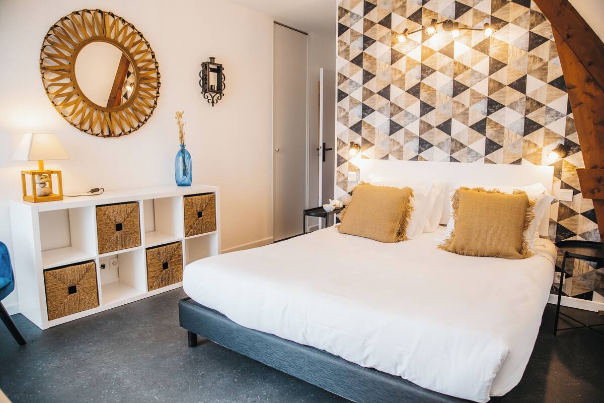 A bedroom with a large bed, a white dresser, a mirror, and a geometric-patterned wall.