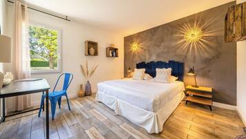 Quarto com cama, mesa de cabeceira, abajur, cadeira e vista para o exterior.