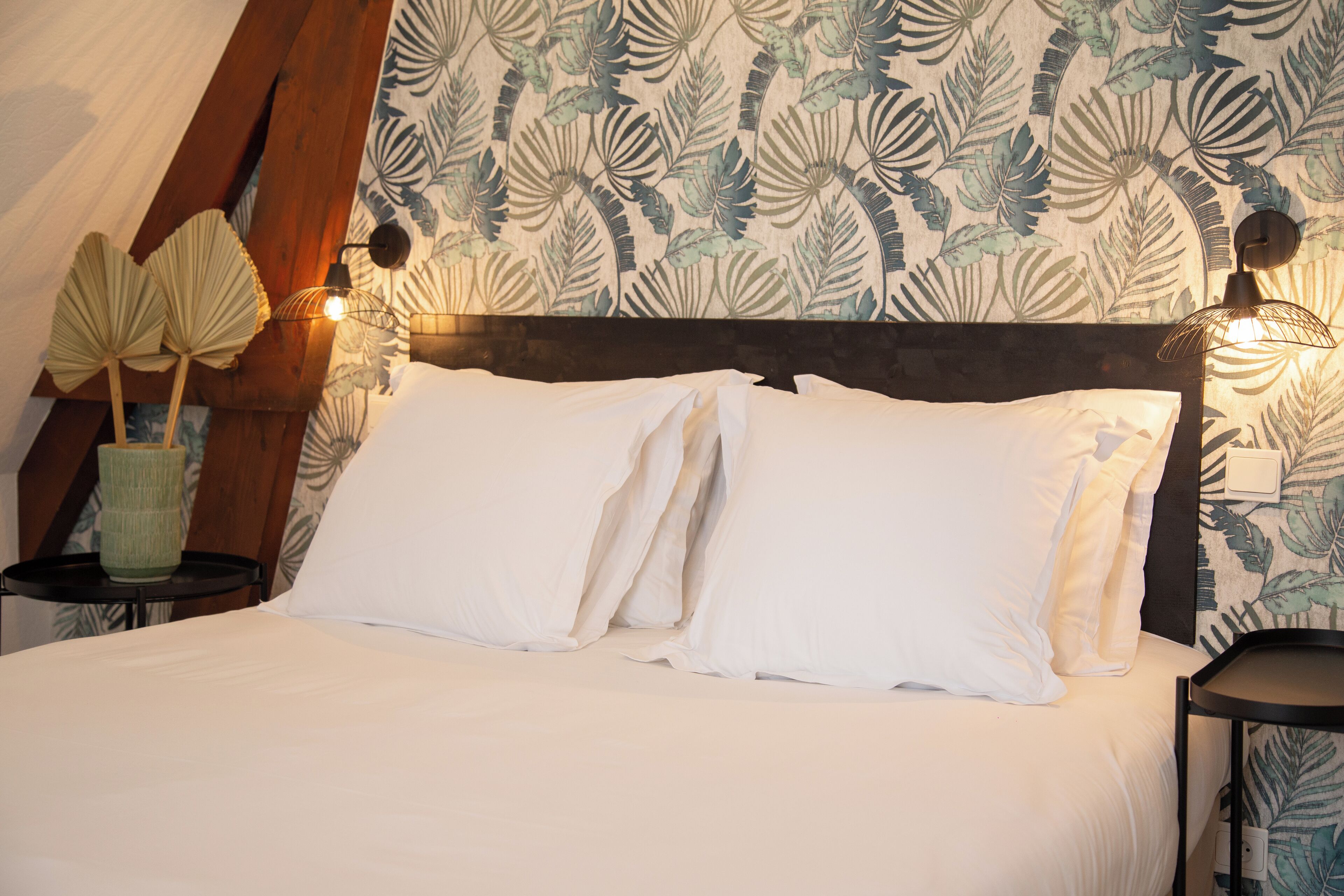 A neatly made bed with white linens, a floral wallpaper pattern, and two wall-mounted lamps on either side.