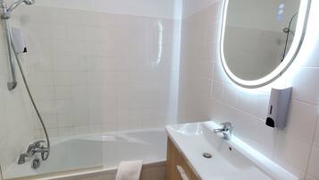 Une salle de bain moderne avec une baignoire entourée de parois en verre, un meuble-lavabo en bois avec un vasque blanche et un miroir mural doté d’un éclairage intégré.