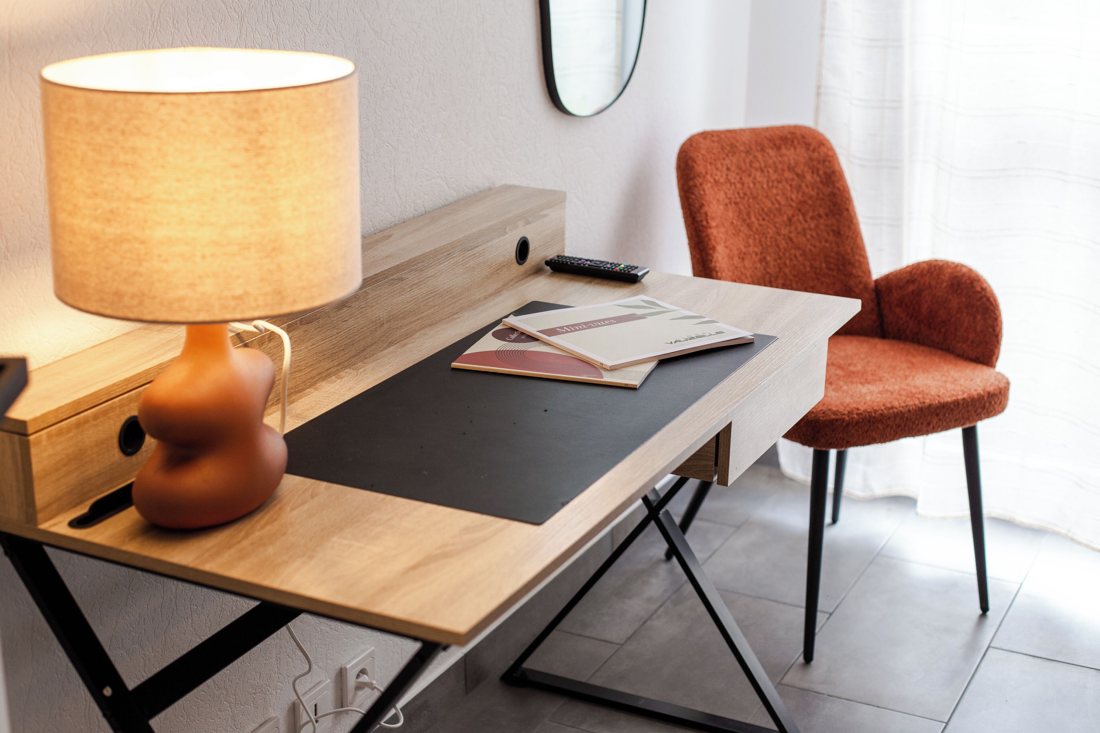A modern room with a wooden desk, a lamp, a chair, and a remote control.