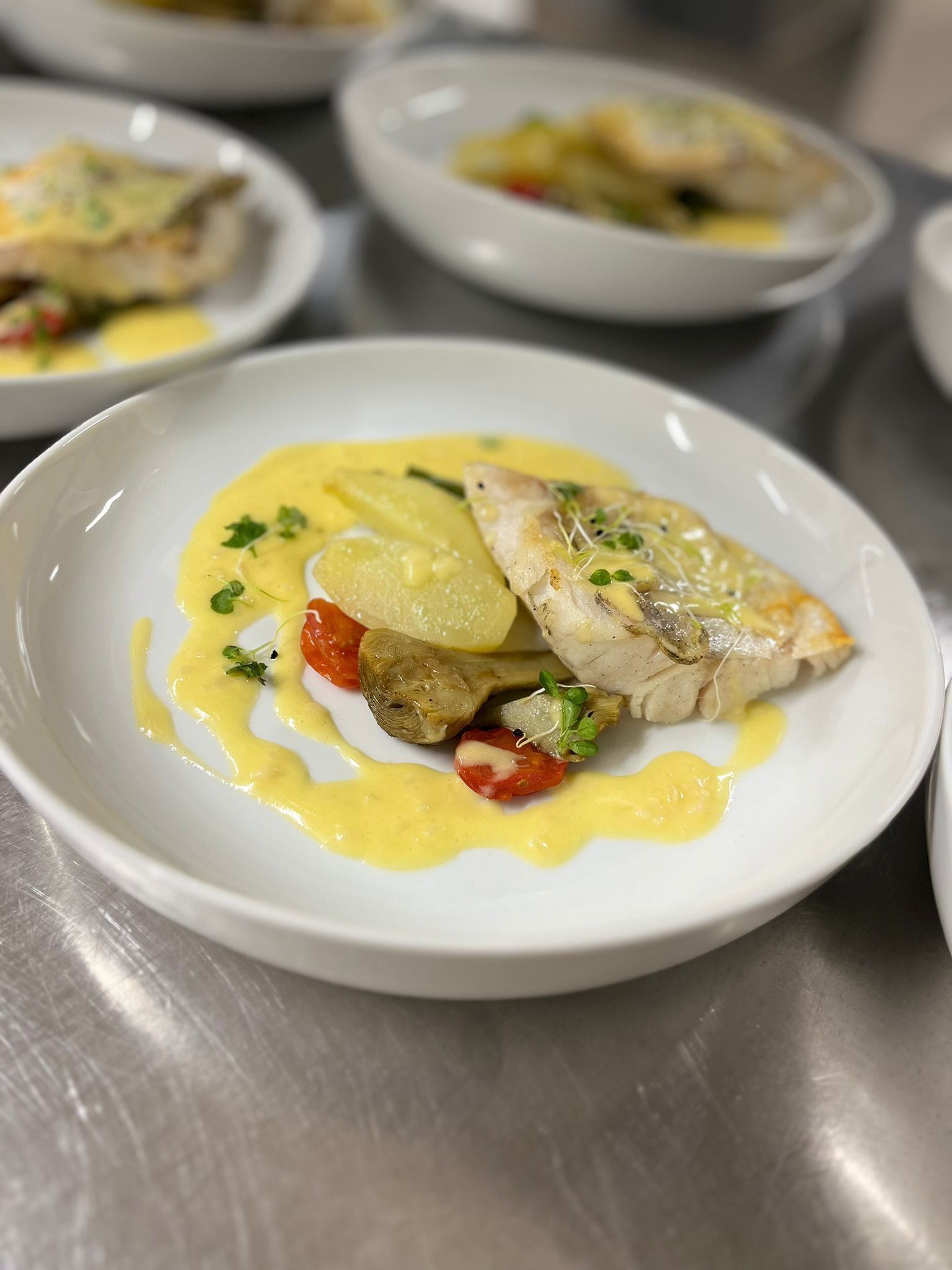 Une assiette de nourriture comprenant du poisson, des pommes de terre et des tomates, servie dans une assiette blanche.