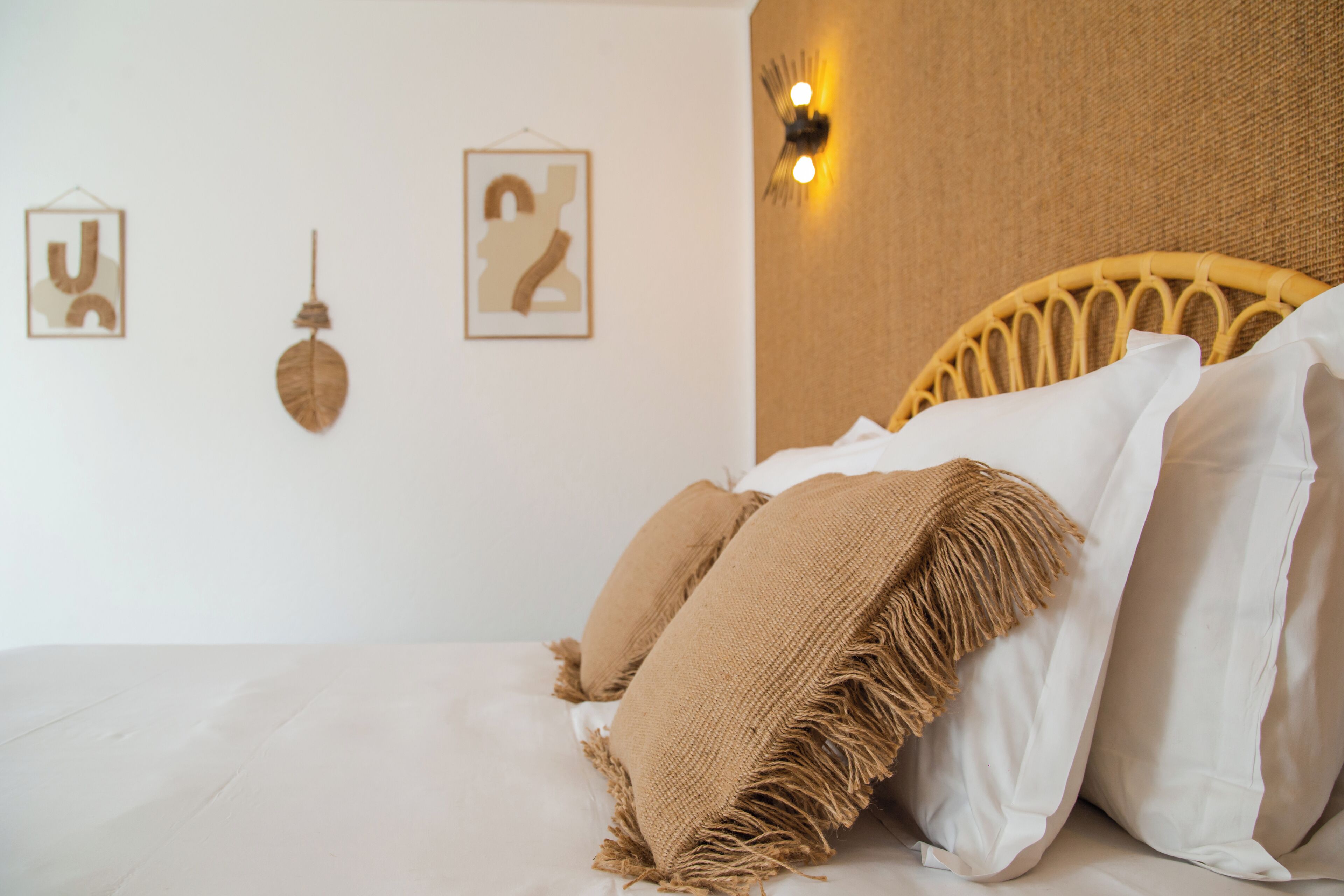 A bed with white linens, a woven headboard, and two framed wall art pieces.