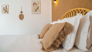 A bed with white linens, a woven headboard, and two framed wall art pieces.