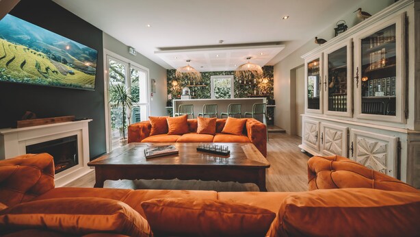 Ein modernes Wohnzimmer mit einem großen Flachbildfernseher, orangefarbenen Sofas, einem Holztisch und einem Kamin.