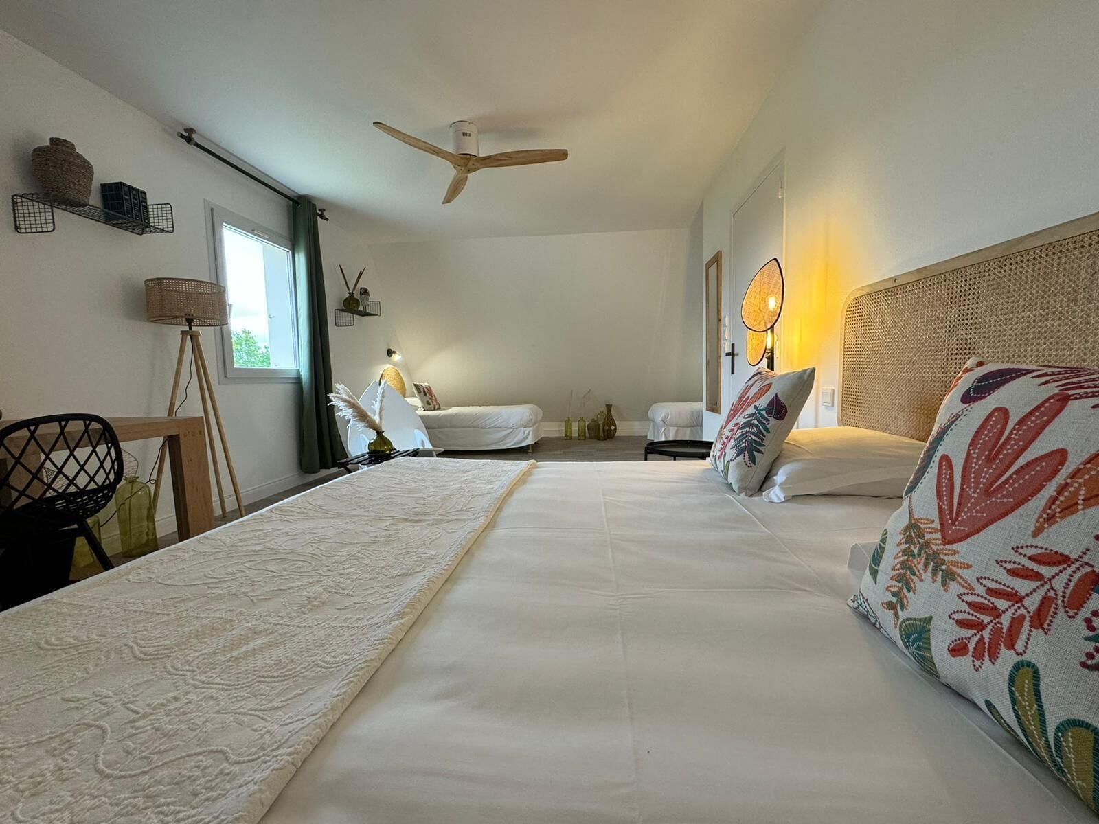 Ein Schlafzimmer mit zwei Betten, einem Deckenventilator, einer Nachttischlampe und Blick ins Freie.