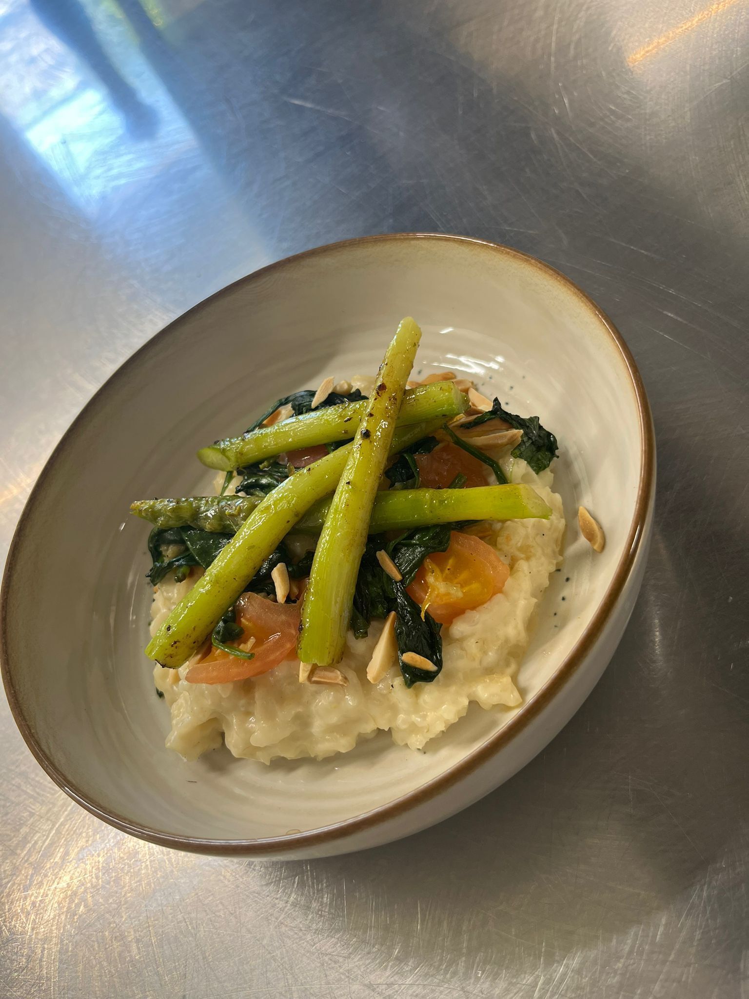 Un tazón de arroz con vegetales y nueces sobre una superficie metálica.