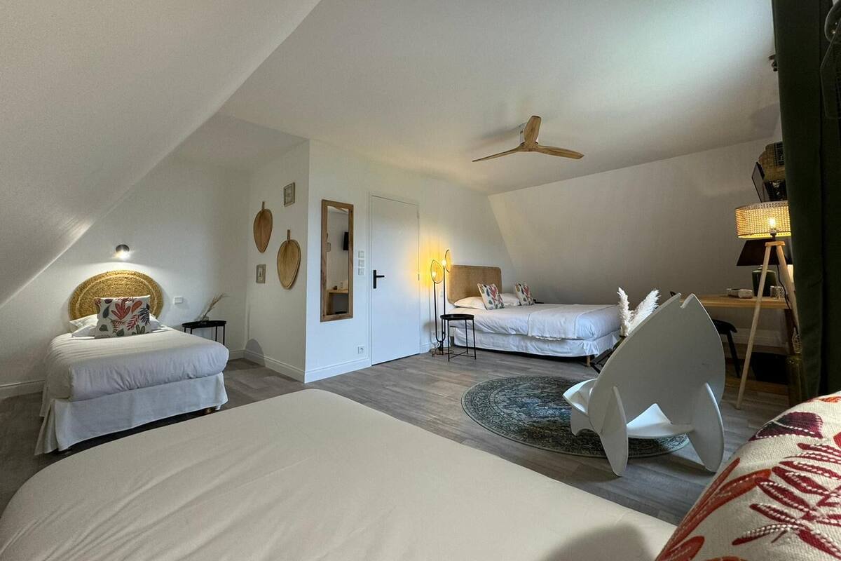 A spacious loft bedroom with a sloped ceiling, a ceiling fan, a large bed, a smaller bed, a desk, and a chair.