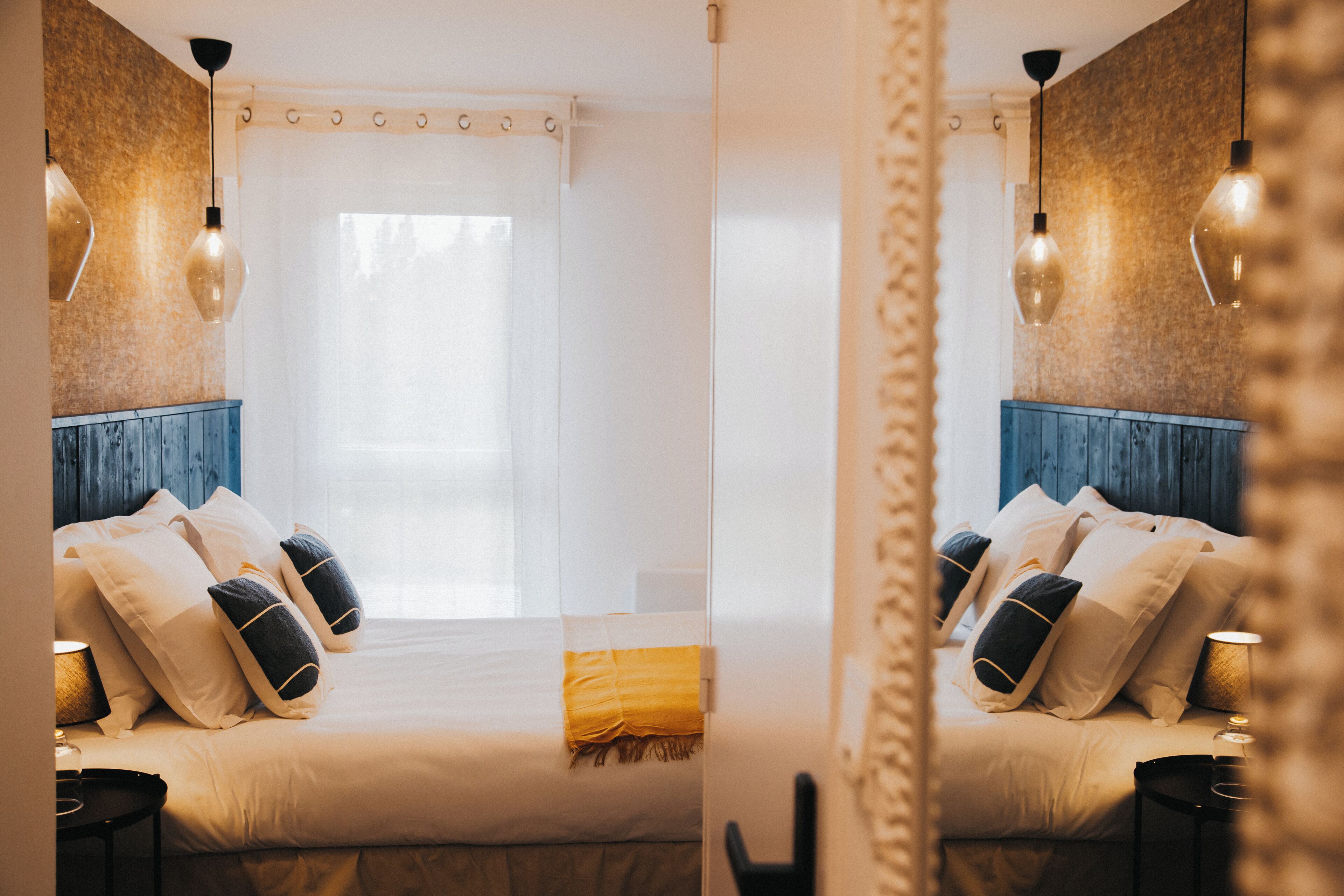Habitación con espejo, cama, almohadas y mesitas de noche.