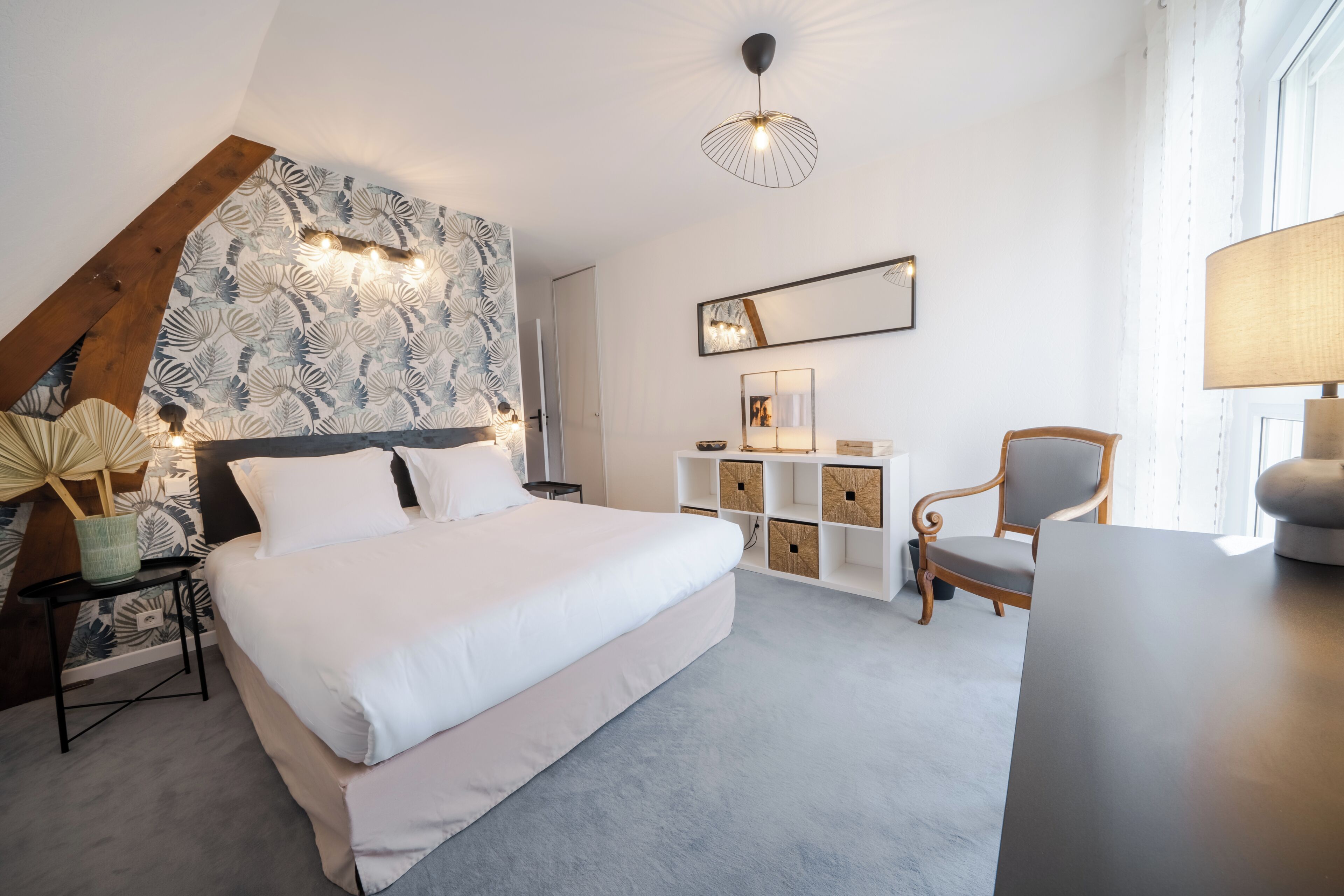 A modern bedroom with a large bed, a wooden headboard, a built-in shelf unit, a chair, and a desk.