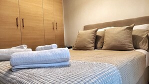 A bedroom with a bed, pillows, a blanket, a wooden wardrobe, and a ceiling light.