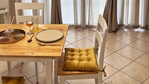 A dining area with a wooden table set for two, a chair with a yellow cushion, and a window with curtains.
