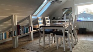 A cozy attic room with a sloped ceiling, a skylight, a dining table with chairs, a bookshelf, and a radiator. - Meer-als Dänemark (Skovby)