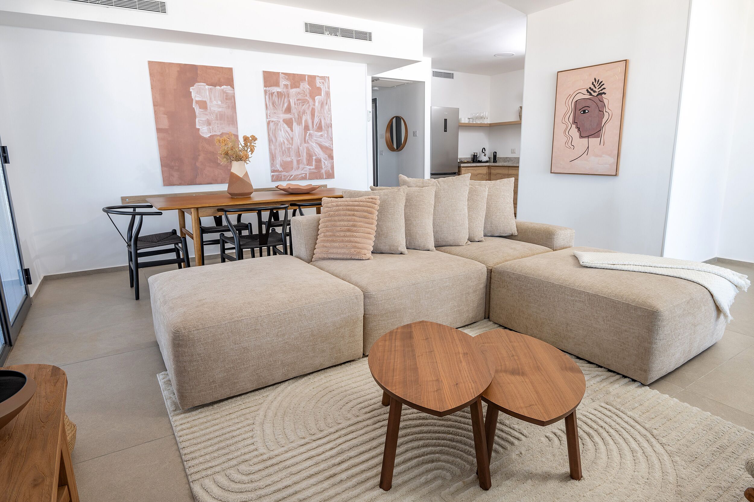 A modern living room with a sectional sofa, a dining table with chairs, and a kitchen in the background.