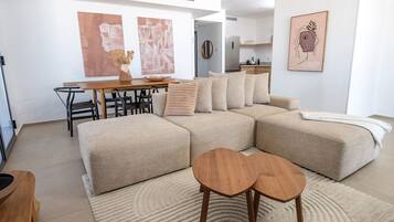 A modern living room with a sectional sofa, a dining table with chairs, and a kitchen in the background.