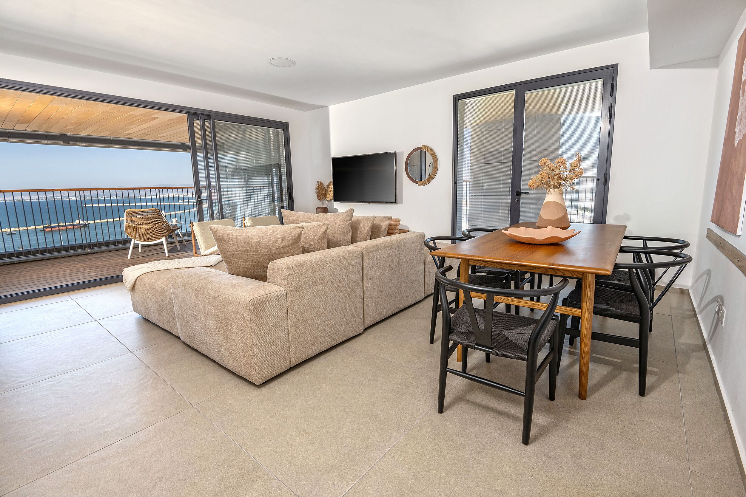Un salon moderne comprenant un canapé, une table à manger, des chaises, un téléviseur et un balcon avec vue sur la mer.