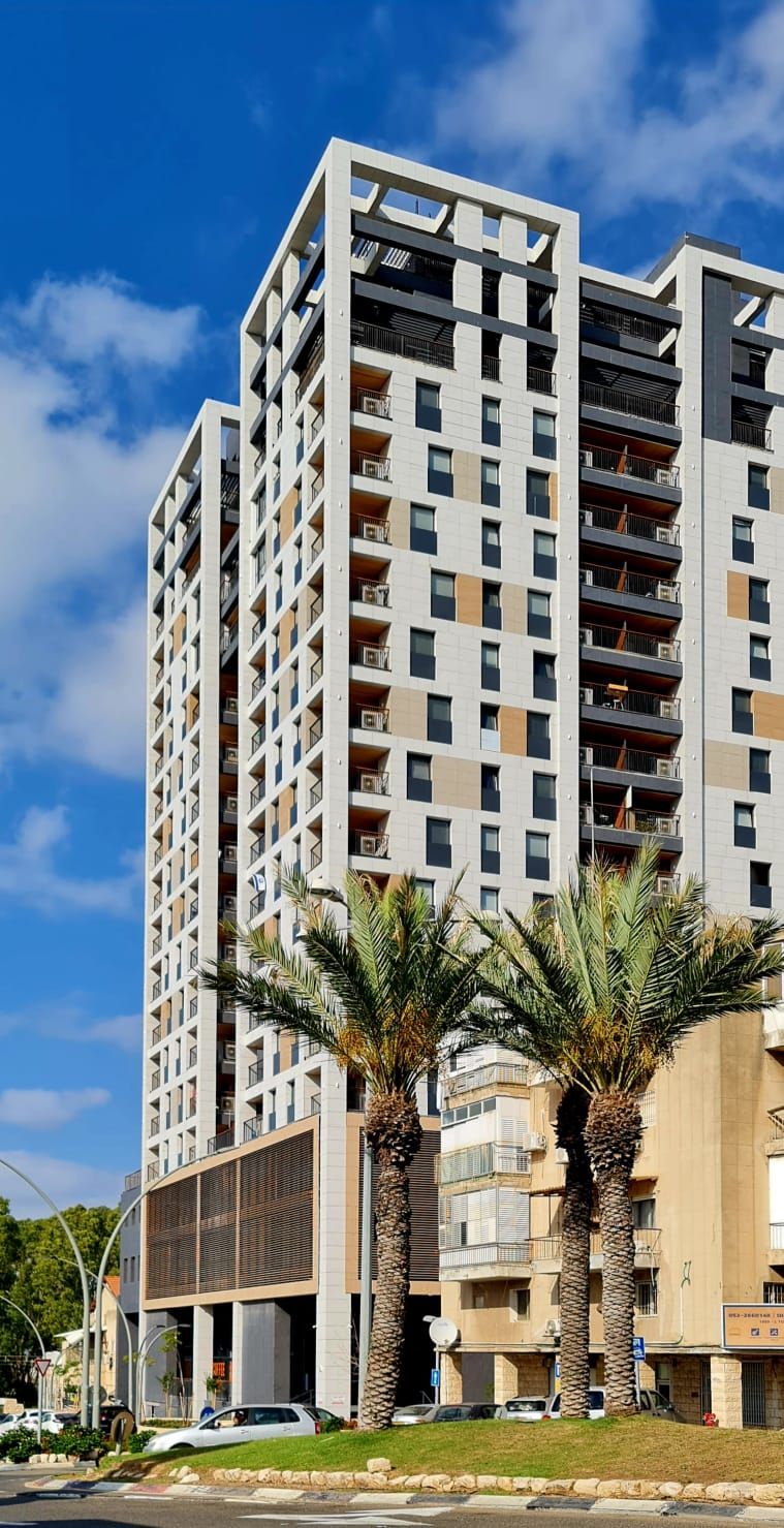 Un immeuble résidentiel à plusieurs étages, doté de balcons, d’un toit plat et de palmiers à l’avant.
