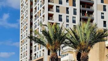 Un immeuble résidentiel à plusieurs étages, doté de balcons, d’un toit plat et de palmiers à l’avant.